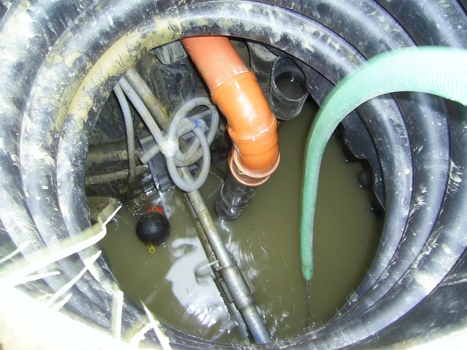 Blick in einen Kanalschacht mit Rohren, Schläuchen und stehendem Wasser